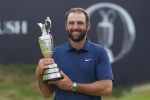 Scottie Scheffler smiling with the British Open Trophy in hands, turned to the left in front of the British Open banner.